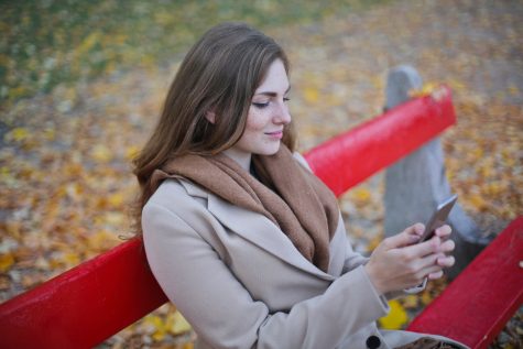 Brunette woman sitting on a red coloured park bench using a mobile phone